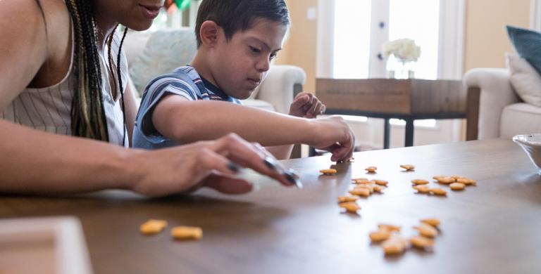 Woman working with young boy with disabilities sorting Goldfish crackers